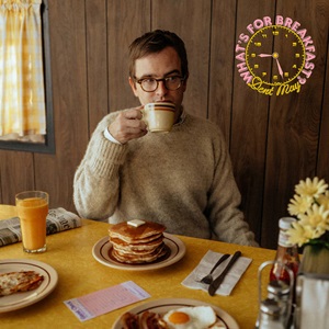 What's For Breakfast album cover. Dent May sitting at a table in the center of the frame with various breakfast foods sprawled out in front of him